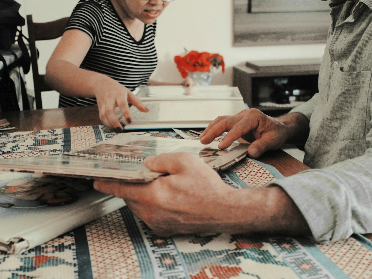 An older person's hands passing a book across a table to a younger person