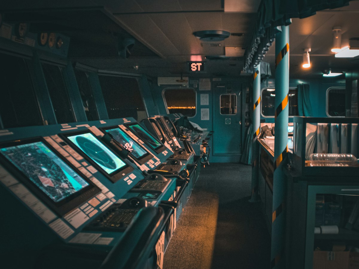 A ship's bridge at night, its navigation consoles lit